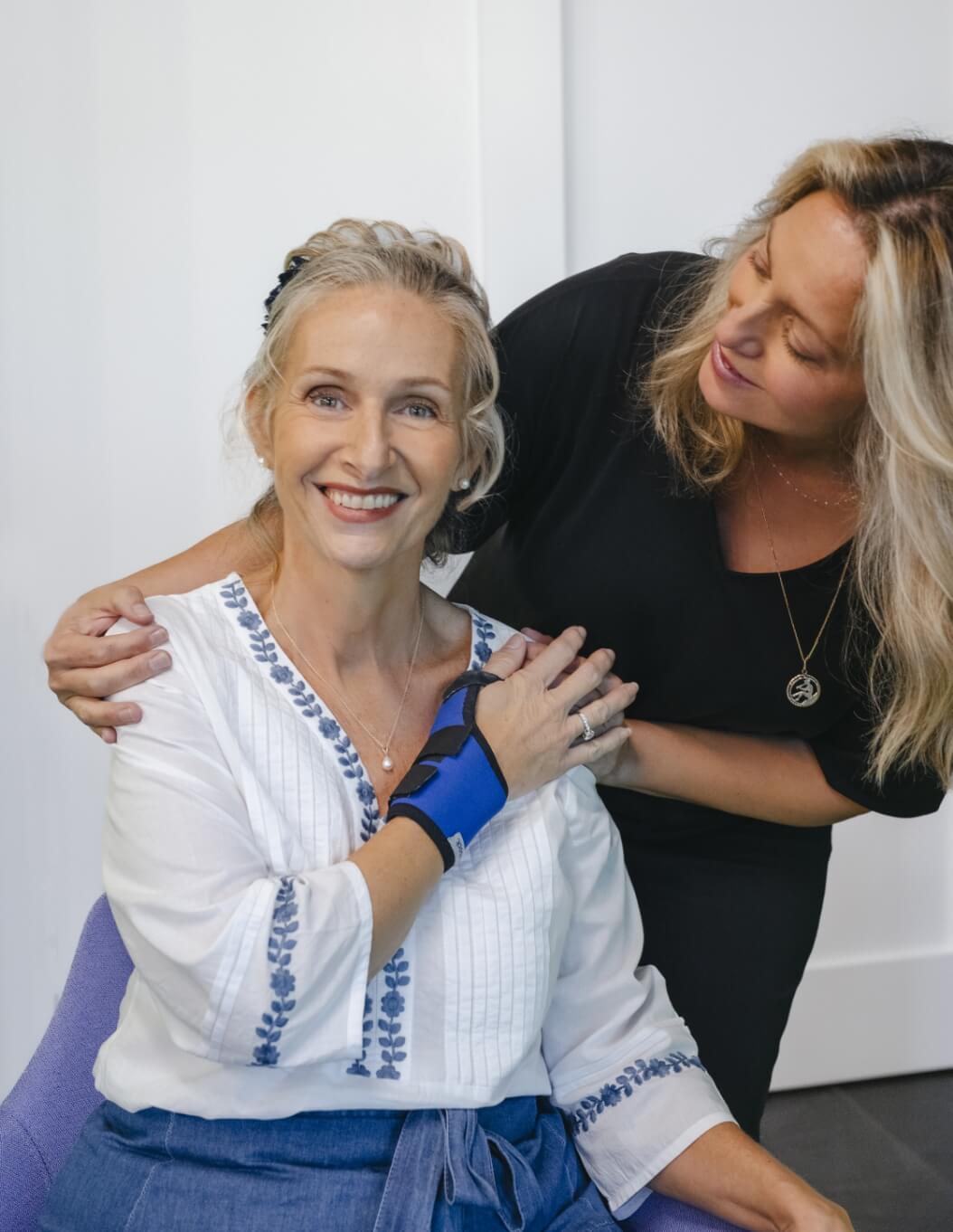 A seated woman holds the hand of a standing woman behind her.